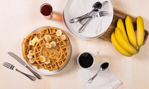 Une table en bois dressée pour le petit-déjeuner, avec des gaufres, des bananes, du sirop, du café et des couverts.