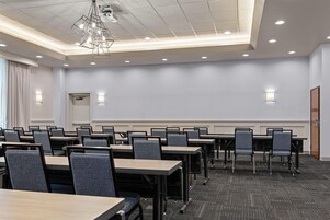 Un salón de conferencias con varias mesas y sillas, una lámpara en el techo y una puerta.