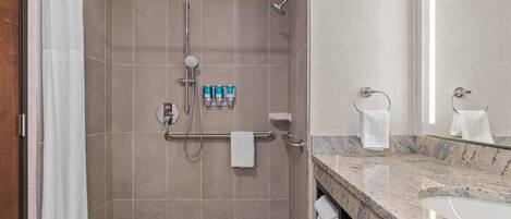 A modern bathroom with a walk-in shower, grab bars, a towel rack, and a marble sink.