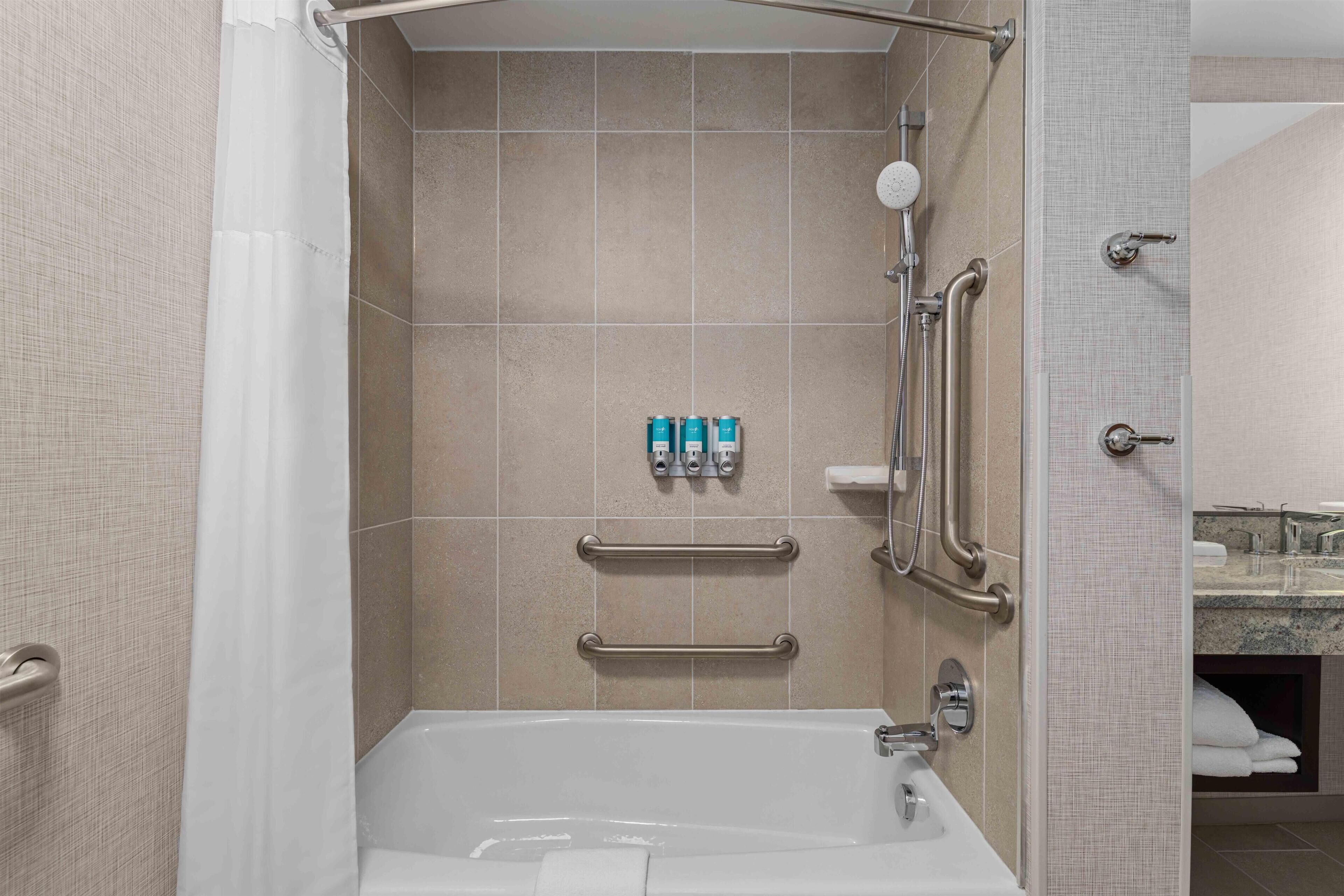 Une salle de bain moderne équipée d’une baignoire, de barres d’appui et d’une douche avec un pommeau de douche amovible.