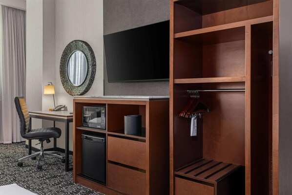 Habitación de hotel con escritorio, silla, televisor, armario y espejo.