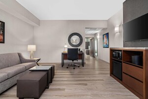 Habitación de hotel moderna con sofá, escritorio, silla, televisor y zona de cocina.