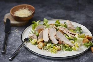 Une assiette de viande tranchée, accompagnée de croûtons et de laitue, posée sur une surface sombre.
