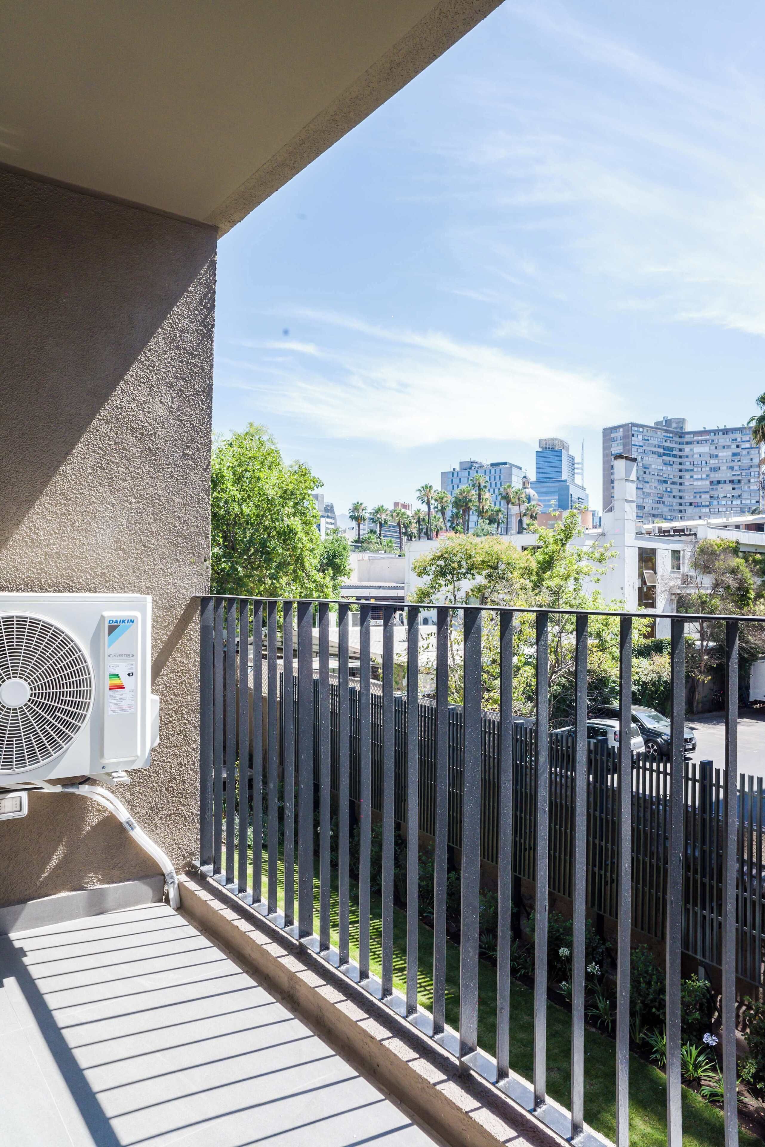 Ein Balkon mit Blick auf eine Stadtlandschaft, einem schwarzen Metallzaun und einer Klimaanlage.