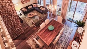 A spacious living area with a large wooden dining table, a dark leather sofa, and a stone accent wall. - Spacious Designer Stay Near Callaway Waterpark (Pine Mountain)
