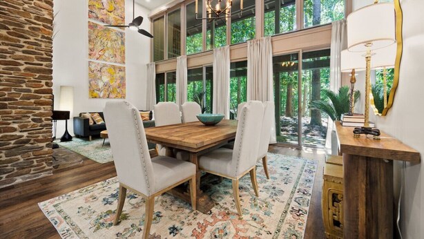 A dining area with a wooden table, white upholstered chairs, and a large window with a view of greenery. - Spacious Designer Stay Near Callaway Waterpark (Pine Mountain)