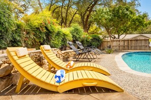 A poolside area with yellow lounge chairs, a stone wall, and a wooden fence. - Modern Family Retreat - Private Pool/Mini Golf/Fire Pit/Pool Table - Sleeps 14 (San Antonio)