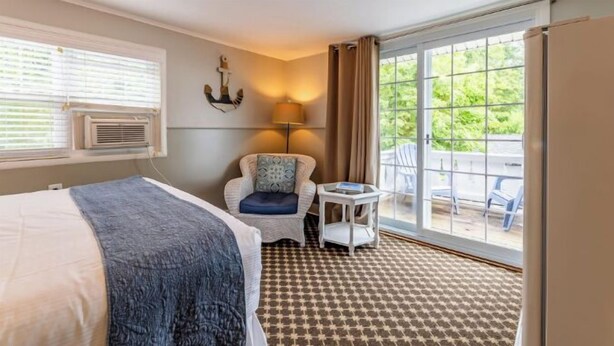 A hotel room with a bed, a chair, a small table, and a large window with a view of greenery.