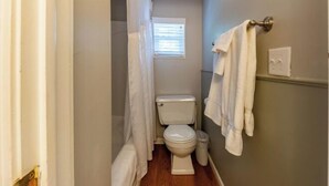 A small, narrow bathroom with a toilet, a window with blinds, and a towel rack with towels.