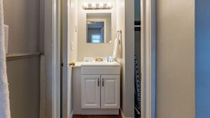 A narrow hallway leading to a bathroom with a vanity, mirror, and lights.