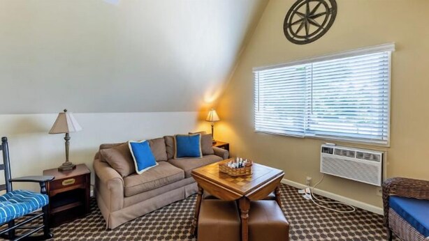 A cozy living area with a sofa, a small table, a lamp, and a window with blinds. - Top Floor Chalet that sleeps large groups (Whitehall)