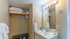 A bathroom with a sink, mirror, and towel rack. There is a shelf above the sink holding towels.