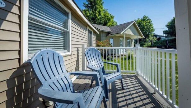 A covered porch with two Adirondack chairs, a white fence, and a house with beige siding and a dark roof.