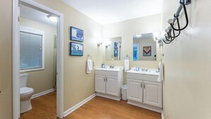 Un baño con dos lavamanos, un inodoro y una ducha. Hay dos cuadros en la pared.
