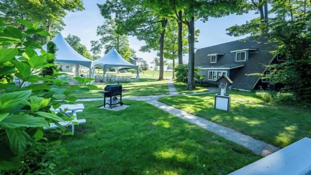 A grassy outdoor area with a barbecue setup, a white gazebo, and a house with a sloped roof. - Cottage F - Great for families, convenient kitchen, and two bedrooms (Whitehall)