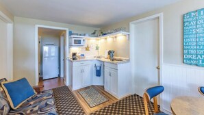 A compact kitchen with white cabinets, a microwave, and a coffee maker. There is a small dining area with a table and two chairs. - Cottage F - Great for families, convenient kitchen, and two bedrooms (Whitehall)