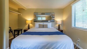 A hotel room with a large bed, two bedside tables with lamps, a headboard with a mirror, and a window with blinds. - Cottage F - Great for families, convenient kitchen, and two bedrooms (Whitehall)