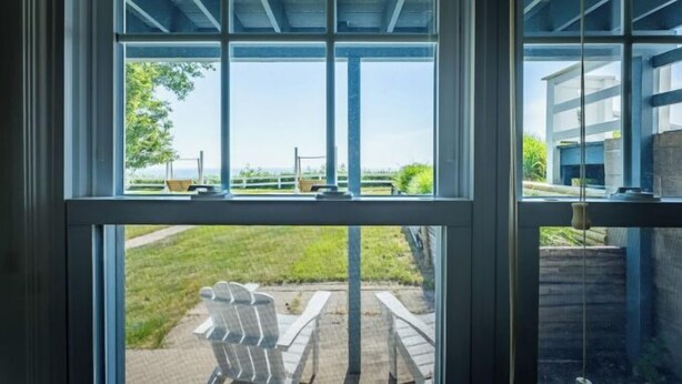 Vista a través de una ventana con marco metálico, un área verde y una silla blanca en el exterior.