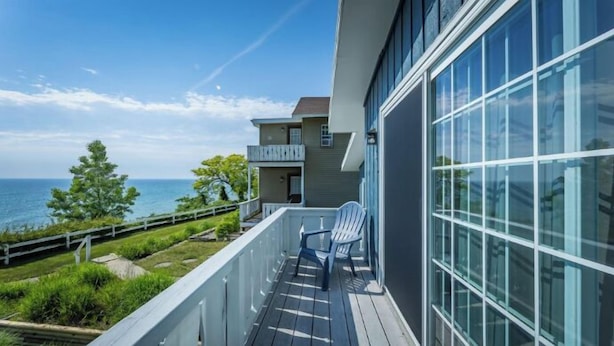 A balcony with a view of the sea, a chair, and a building with large windows. - Lakefront King with full kitchen (Whitehall)
