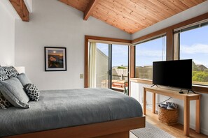 Ein Schlafzimmer mit einem Bett, einem Fernseher auf einem Holztisch, einem Fenster mit Blick und einem gerahmten Bild an der Wand.