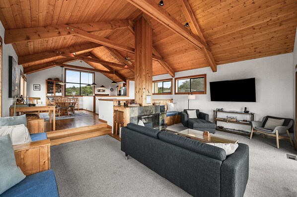 Een ruime woonkamer met een hoge plafond, een open haard, een televisie en een eethoek met natuurlijk licht.