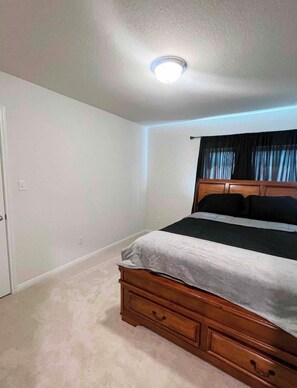 A bedroom with a wooden bed, a white ceiling light, and a door. - Spacious 4-bedroom house in fabulous Kyle with AC comfort (Kyle)