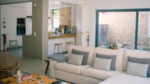 Ein modernes Wohnzimmer mit einem beigefarbenen Sofa, einem Holztisch und Blick auf eine Steinsäule durch ein großes Fenster.