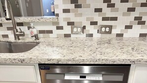Una cocina moderna con lavavajillas de acero inoxidable, armarios blancos y salpicadero de azulejos.