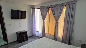 Una camera da letto con un letto, una TV a parete, una cassettiera e una finestra con tende.