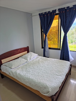 A bed with a wooden headboard, a window with curtains, and a view of greenery outside.