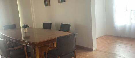 Una habitación amplia con una gran mesa de madera para comer, varias sillas y una planta en maceta.