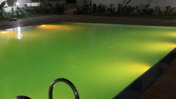 Vista nocturna de una piscina con tonalidades verdes, rodeada por un edificio de varios pisos con balcones.