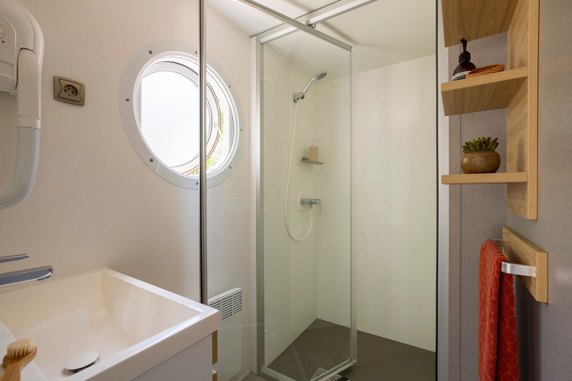 The modern bathroom features a sleek shower with a round window, creating a bright and airy atmosphere that complements the mobile home’s coastal charm.