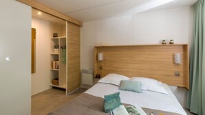 Una camera d'albergo moderna con una testiera in legno, un letto grande con lenzuola bianche, un comodino con una lampada e un armadio a muro con ripiani.