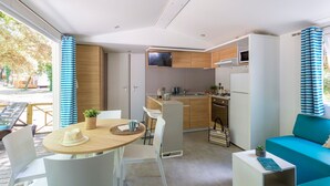 Una cucina compatta con elettrodomestici moderni, un'area pranzo con tavolo e sedie rotonde, e un angolo salotto accogliente con un divano color petrolio.