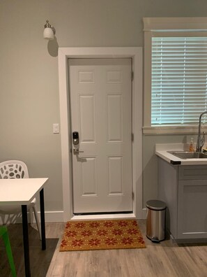 A kitchen with a white door, a window with blinds, a sink, and a trash can. - Beautiful 1b1b sitting at the centre of the City of Richmond for rent(Long Term) (Richmond)