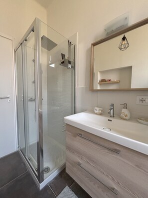 Une salle de bain moderne avec une douche à parois de verre, un meuble-lavabo blanc avec un miroir et un meuble en bois.
