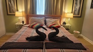 Une chambre d’hôtel avec un lit, des oreillers, une table de chevet avec une lampe, une horloge et une poubelle.
