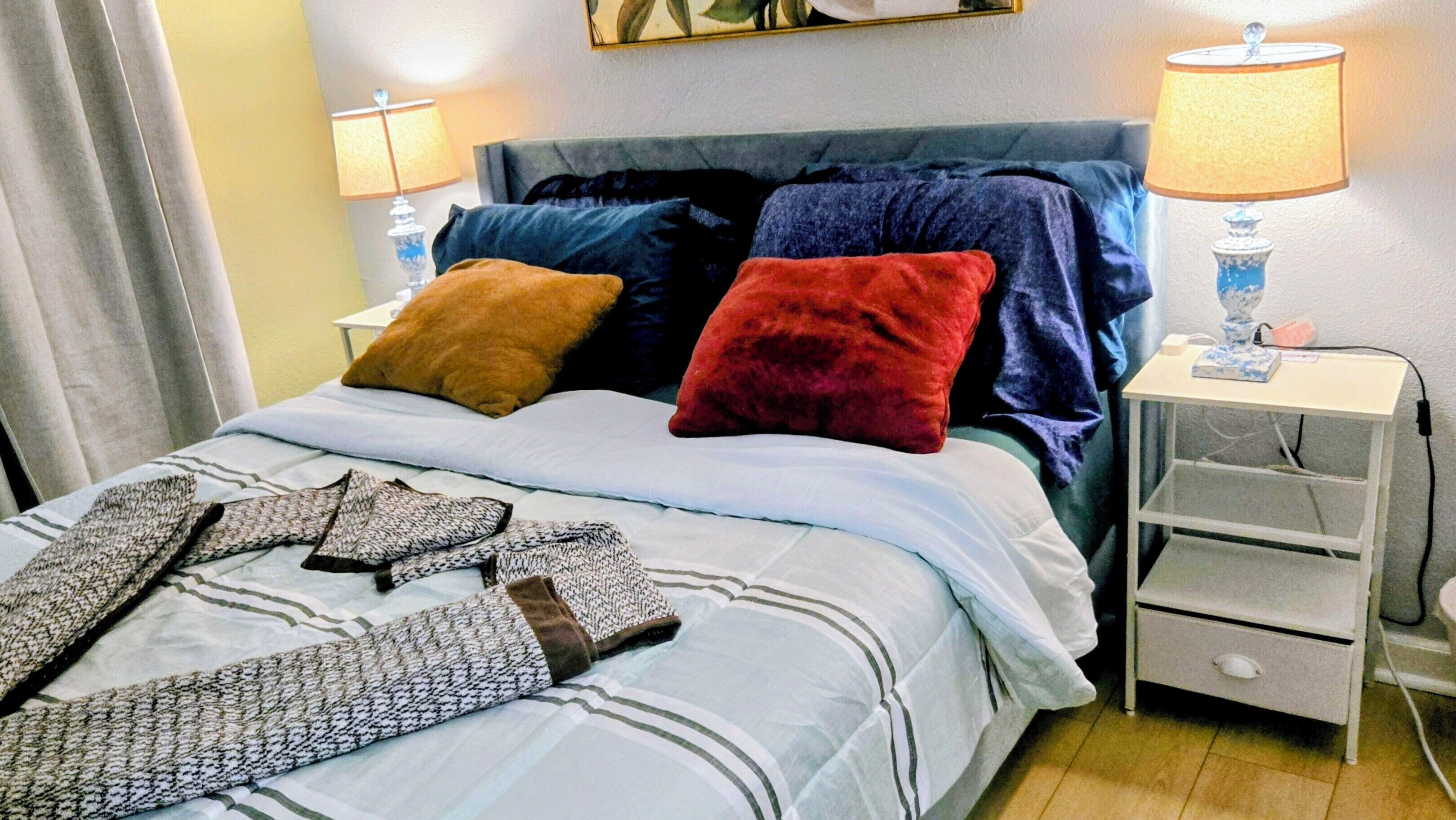 Un lit avec une couvre-lit à rayures, deux oreillers, une table de chevet avec une lampe et une petite table de nuit avec une lampe.