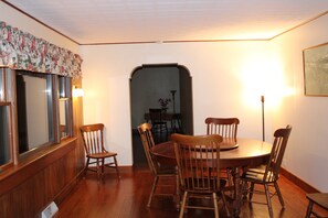 Ein Esszimmer mit Holztisch und -stühlen, einem Fenster mit Vorhängen sowie einer Lampe.