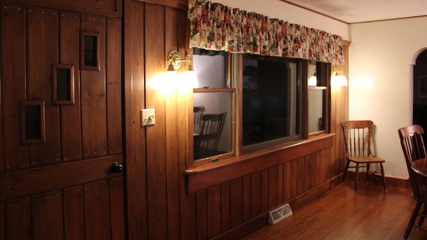 Una habitación con paneles de madera, un ventanal grande, dos lámparas de pared y una silla.