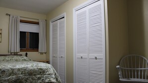 Un dormitorio con una cama, una silla y dos armarios blancos con puertas a persiana.
