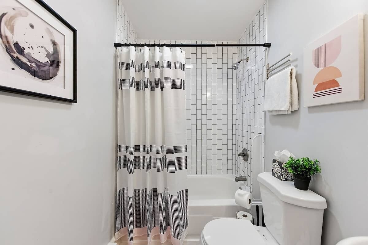 A bathroom with a shower curtain, a toilet, a bathtub, and a small potted plant.