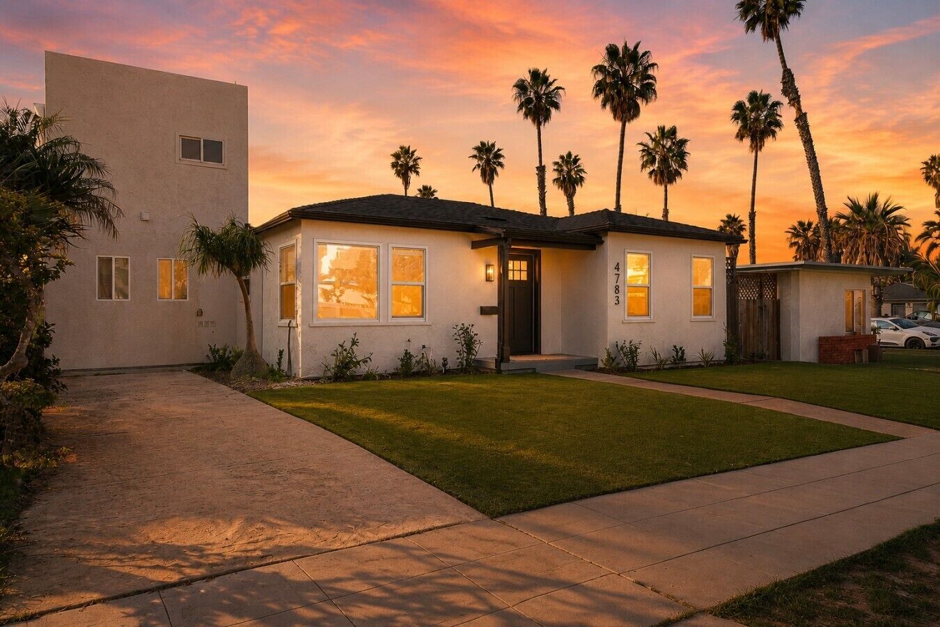 A single-story house with a front yard, palm trees, and a sunset sky.