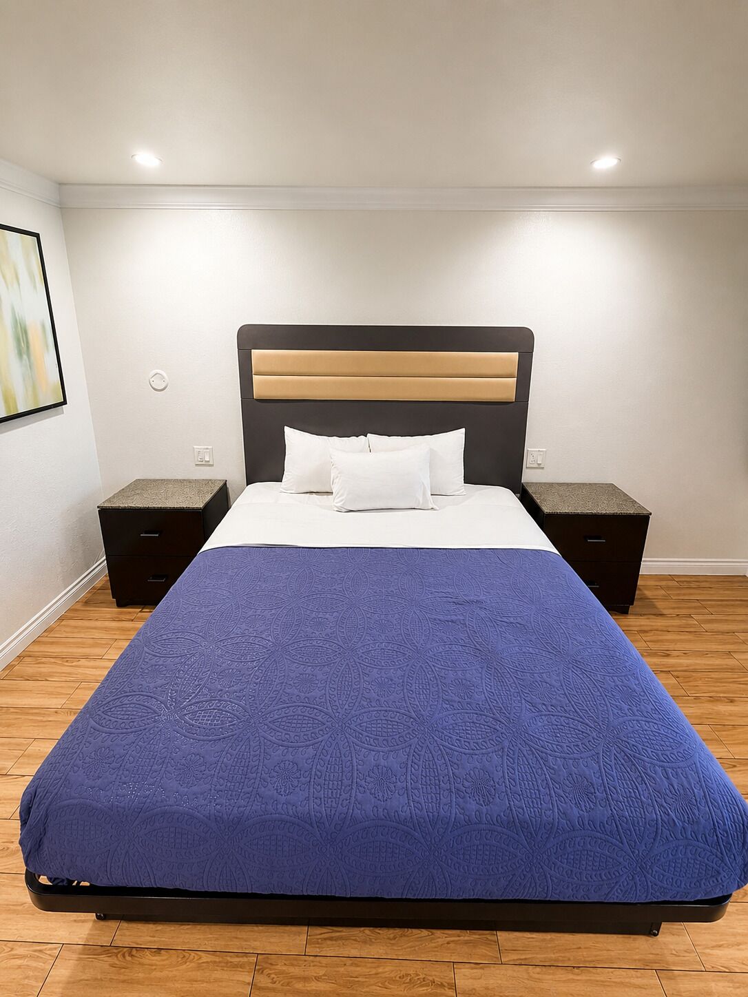 A bed with a blue bedspread, two bedside tables, and a headboard.