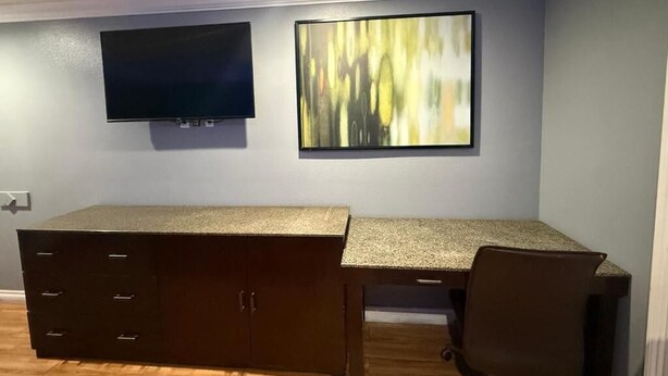 A room with a desk, a chair, a flat-screen TV, and a large abstract painting on the wall. - Bell Resort Motel (Bell Gardens)