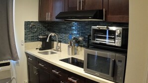 Uma cozinha compacta com armários de madeira escura, micro-ondas de aço inoxidável, forno embutido, coifa preta e painel de azulejos.