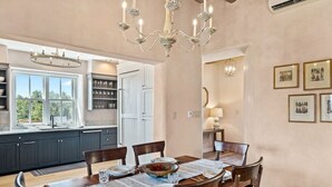 A dining area with a wooden table set for four, surrounded by chairs. There is a chandelier above the table, and a window with a view of greenery outside. - Santa Fe Santuario- Perfect Views, Kiva Fireplace (Santa Fe)