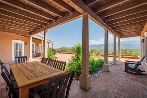 Une terrasse extérieure avec une table et des chaises en bois, entourée d’un sol en briques et de plantes.