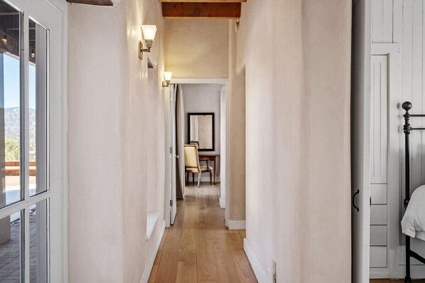 A narrow hallway with a wooden floor, white walls, and a bed with a metal frame on the right. - Santa Fe Santuario- Perfect Views, Kiva Fireplace (Santa Fe)